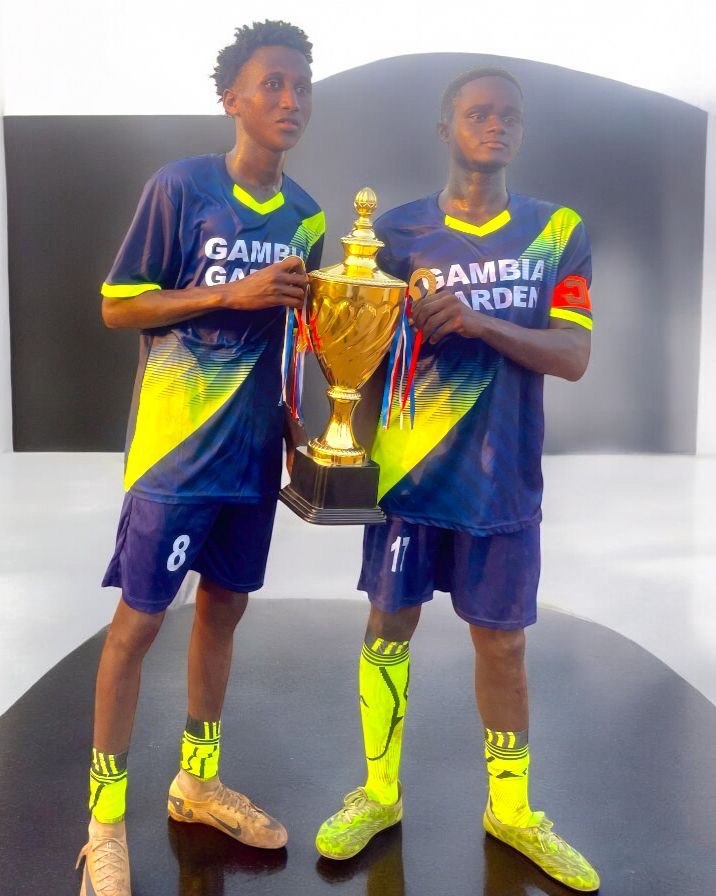 Two players in Gambia Garden jerseys holding a trophy