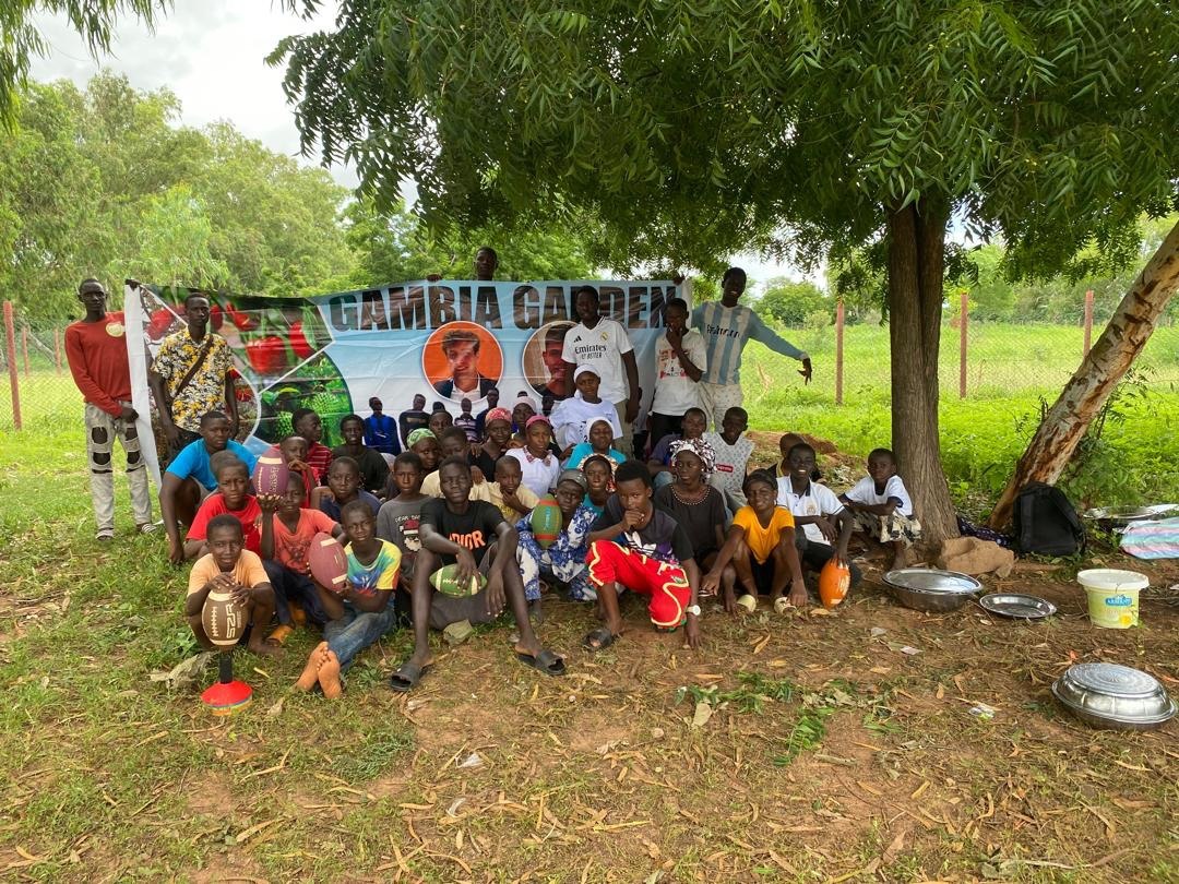 Young players together beneath a Gambia Garden banner